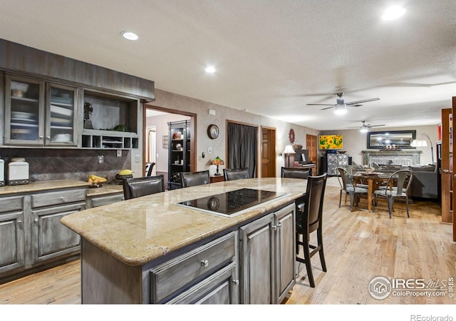 kitchen featuring light wood-style flooring, a center island, black electric stovetop, a fireplace, and backsplash