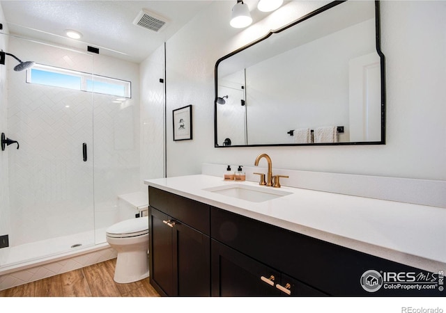 bathroom with visible vents, toilet, wood finished floors, vanity, and a shower stall