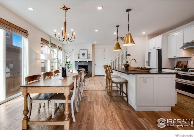 dining space featuring light wood-style floors, recessed lighting, a fireplace, and an inviting chandelier