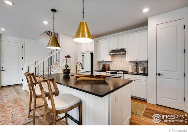 kitchen with high end stove, under cabinet range hood, dark countertops, and light wood finished floors