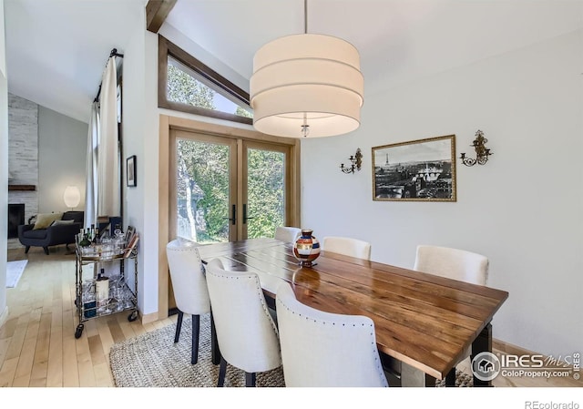 dining room featuring light wood-style flooring, a fireplace, vaulted ceiling, and french doors