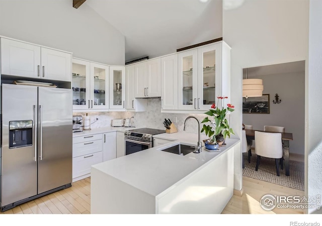 kitchen with stainless steel appliances, lofted ceiling, light countertops, a sink, and a peninsula