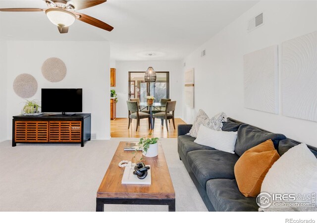 carpeted living area featuring visible vents and a ceiling fan