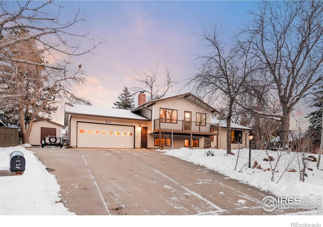 split level home featuring driveway, a storage shed, a chimney, an attached garage, and fence