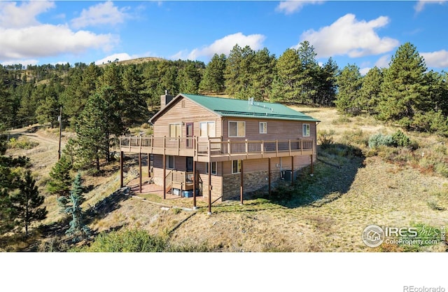 back of property with a chimney, metal roof, a view of trees, cooling unit, and a wooden deck