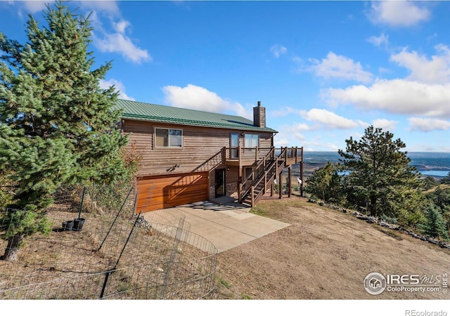 rear view of house with metal roof, stairs, concrete driveway, a wooden deck, and a chimney