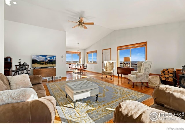 living room featuring visible vents, a wood stove, ceiling fan, vaulted ceiling, and wood finished floors