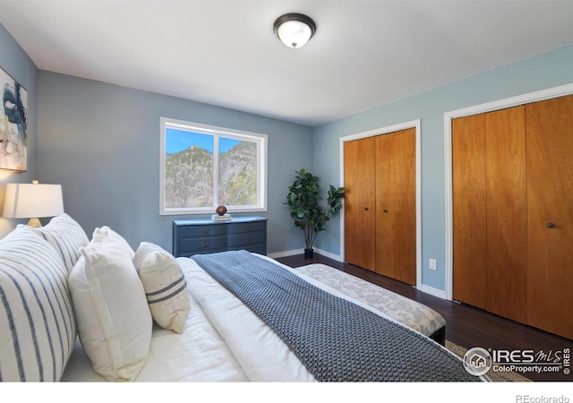 bedroom featuring baseboards, dark wood-style flooring, and multiple closets