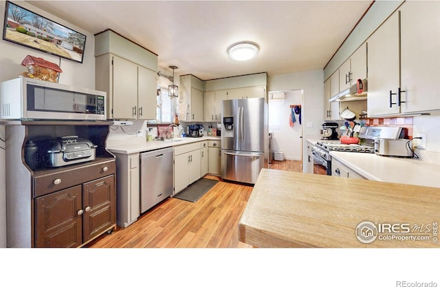 kitchen with under cabinet range hood, light wood-style flooring, appliances with stainless steel finishes, and light countertops