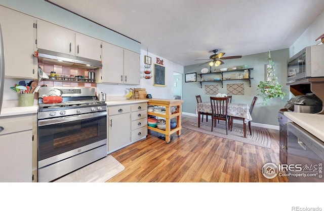 kitchen with stainless steel appliances, light countertops, a ceiling fan, light wood-type flooring, and under cabinet range hood