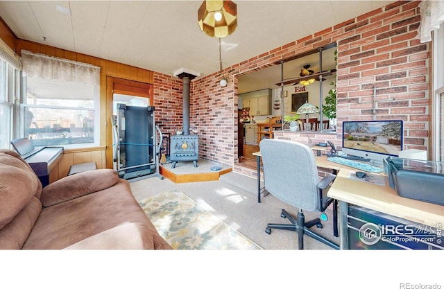 carpeted office space with a wood stove, brick wall, and wooden walls