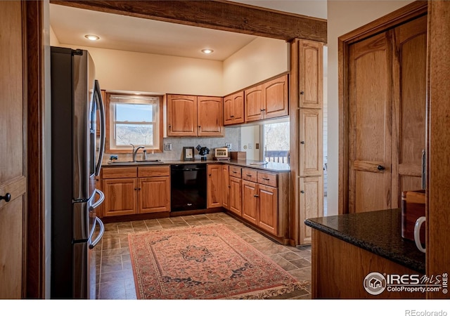 kitchen with a sink, stone finish floor, black dishwasher, stainless steel refrigerator with ice dispenser, and dark countertops