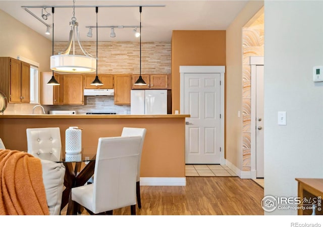 kitchen with under cabinet range hood, light wood-style floors, freestanding refrigerator, decorative backsplash, and pendant lighting