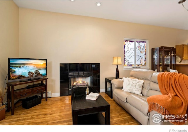 living room featuring light wood-type flooring, baseboards, a tiled fireplace, and recessed lighting