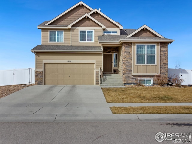 craftsman-style home featuring a garage, concrete driveway, stone siding, a gate, and fence