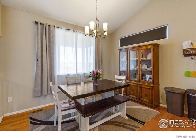 dining area with a notable chandelier, wood finished floors, visible vents, baseboards, and vaulted ceiling