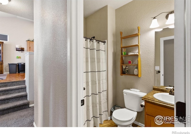 full bathroom featuring a shower with shower curtain, a textured wall, vanity, and toilet