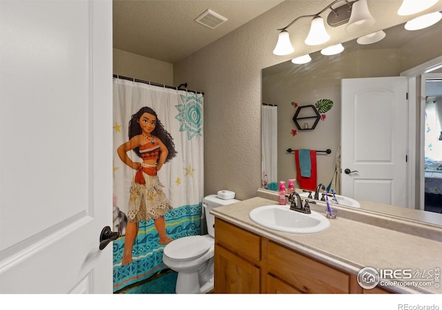 bathroom featuring visible vents, a textured wall, vanity, and toilet