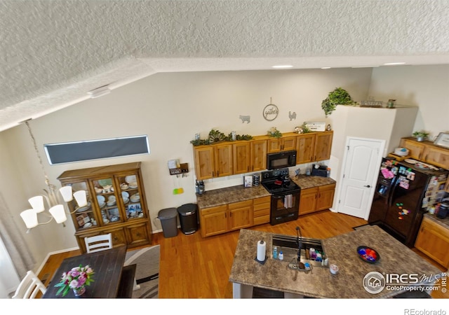 kitchen with lofted ceiling, a textured ceiling, light wood-style flooring, black appliances, and brown cabinetry