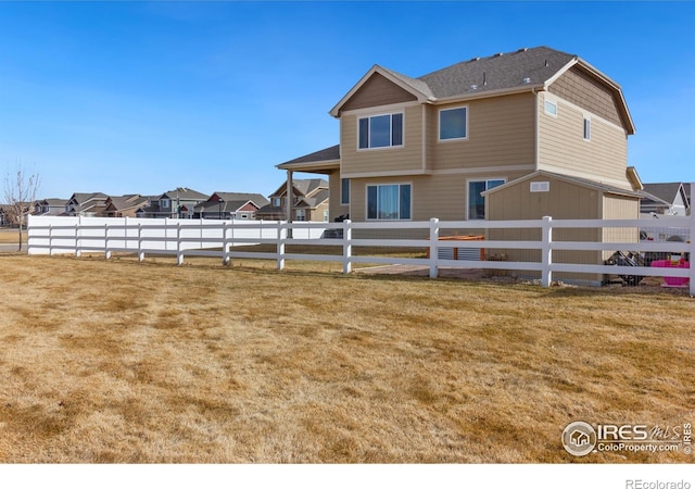 back of house featuring an outbuilding, fence, and a lawn