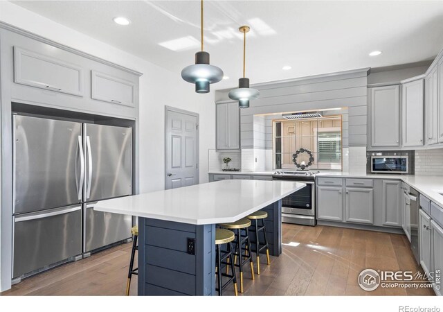 kitchen featuring decorative backsplash, appliances with stainless steel finishes, a breakfast bar area, and hardwood / wood-style flooring