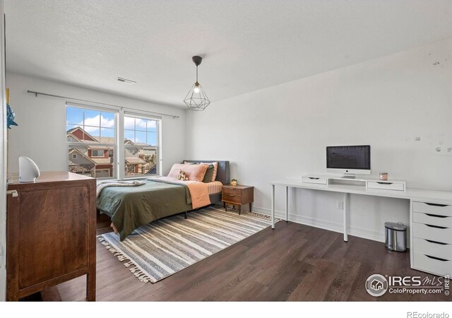 bedroom featuring visible vents, a textured ceiling, baseboards, and wood finished floors