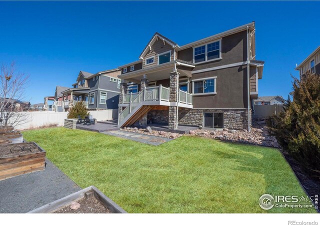 rear view of property featuring fence, stucco siding, stairs, stone siding, and a lawn