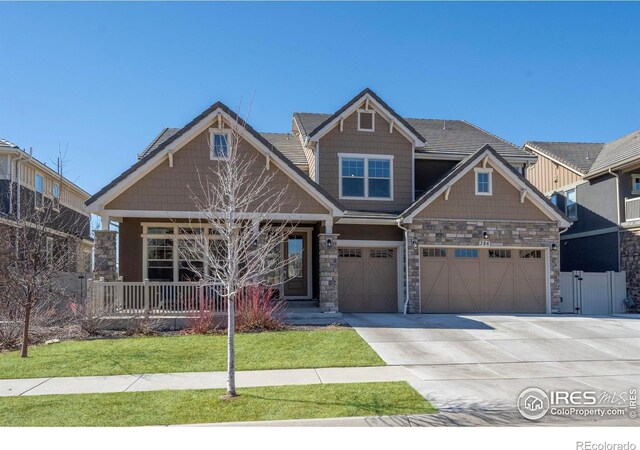 craftsman-style home featuring fence, driveway, covered porch, a front lawn, and stone siding