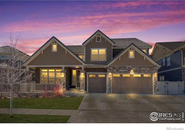 craftsman-style home featuring fence, concrete driveway, covered porch, stone siding, and a gate