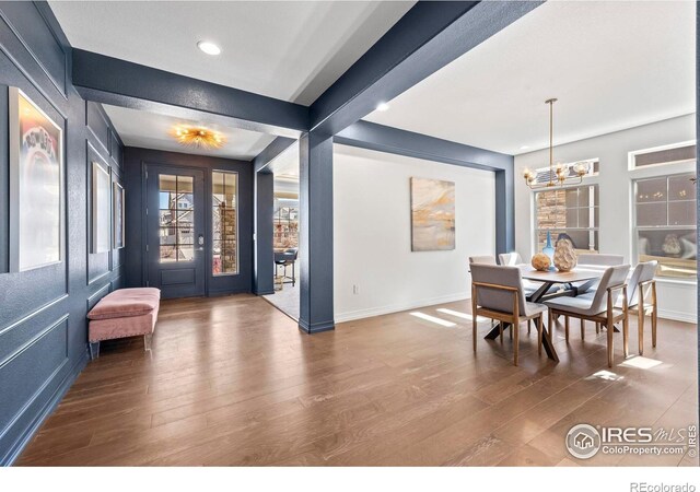 dining area featuring beam ceiling, a notable chandelier, baseboards, and wood finished floors