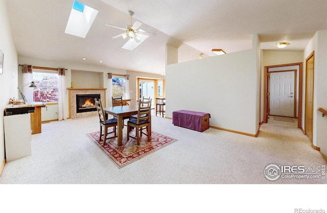 dining area with baseboards, vaulted ceiling with skylight, a tile fireplace, and light colored carpet