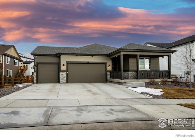 view of front of home featuring an attached garage, covered porch, fence, concrete driveway, and stone siding