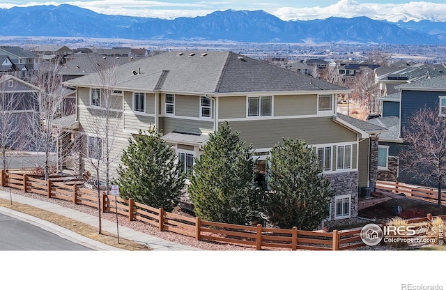 view of front facade with a fenced front yard, a residential view, roof with shingles, and a mountain view