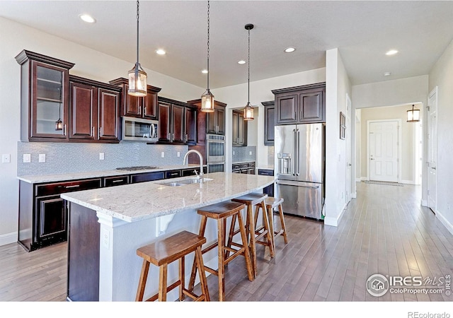 kitchen featuring tasteful backsplash, light wood-style flooring, stainless steel appliances, a kitchen bar, and a sink