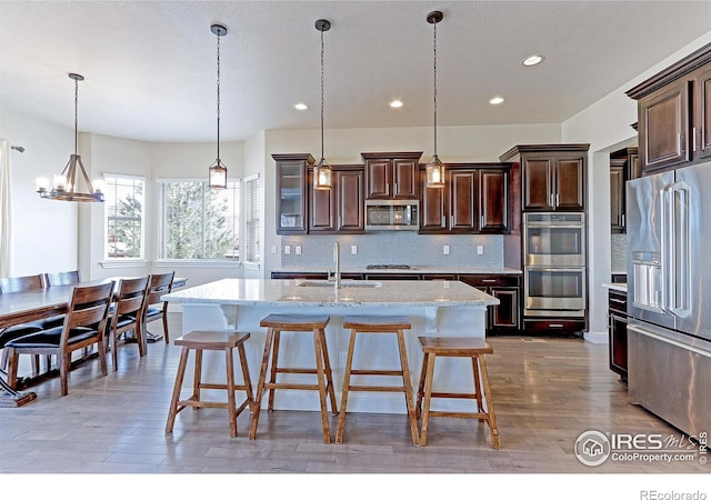 kitchen featuring tasteful backsplash, wood finished floors, light stone countertops, stainless steel appliances, and dark brown cabinets