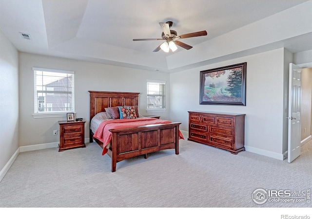 carpeted bedroom featuring a tray ceiling, visible vents, ceiling fan, and baseboards