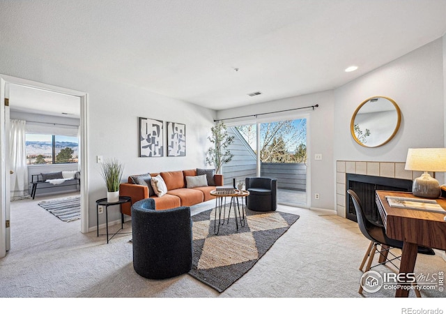 carpeted living area featuring plenty of natural light, visible vents, baseboards, and a tile fireplace