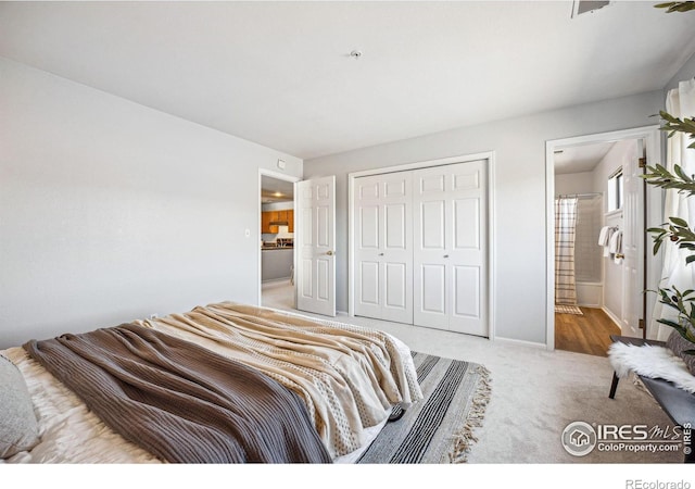 carpeted bedroom featuring a closet, ensuite bath, and baseboards