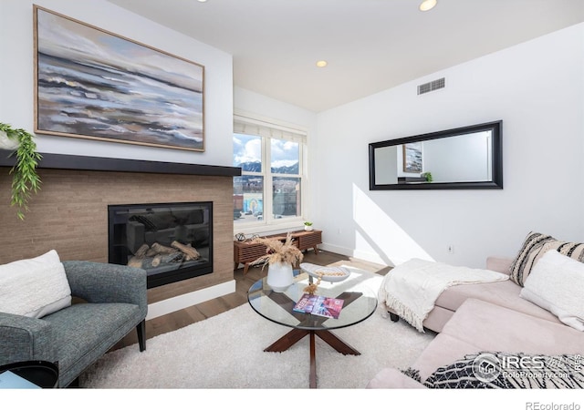 living area featuring baseboards, visible vents, a glass covered fireplace, wood finished floors, and recessed lighting