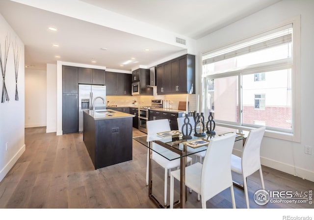 kitchen featuring a center island with sink, tasteful backsplash, appliances with stainless steel finishes, dark brown cabinetry, and a sink