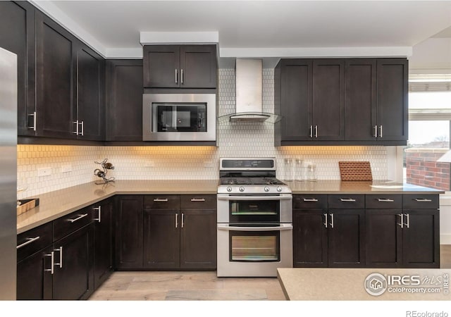 kitchen with stainless steel appliances, light countertops, light wood-style flooring, decorative backsplash, and wall chimney range hood