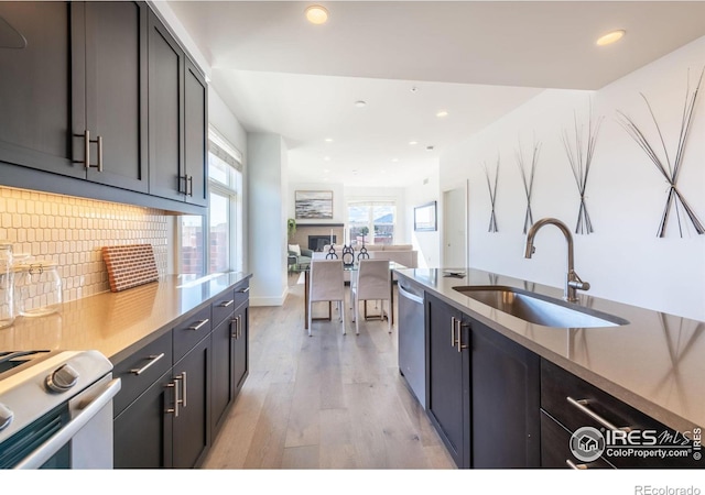 kitchen with light wood-style flooring, a sink, decorative backsplash, dishwasher, and gas range