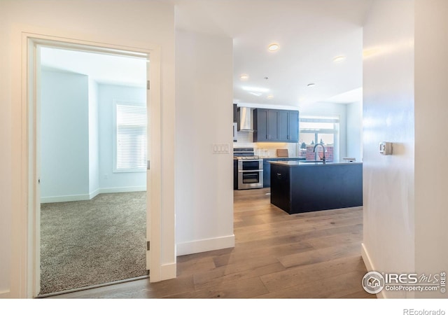 kitchen featuring range with two ovens, light wood finished floors, decorative backsplash, a sink, and wall chimney exhaust hood