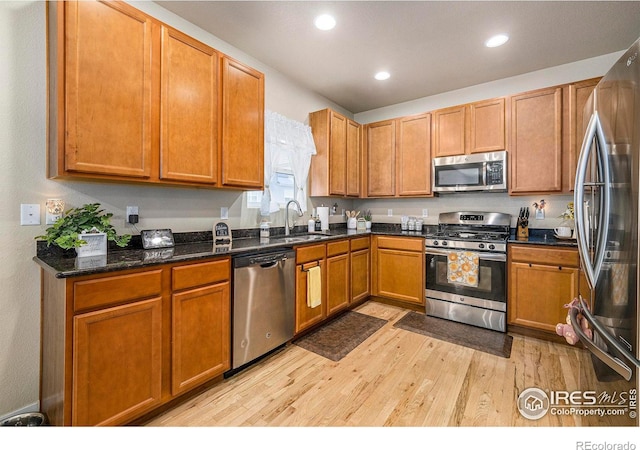 kitchen featuring recessed lighting, stainless steel appliances, a sink, light wood-style floors, and dark stone countertops