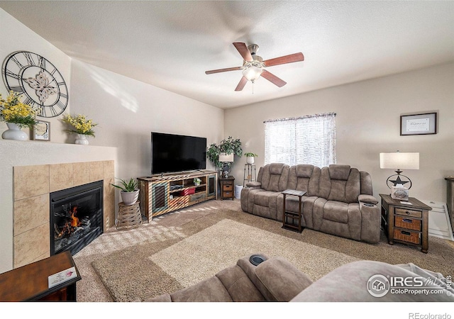 living room featuring ceiling fan, a tile fireplace, carpet flooring, and a textured ceiling