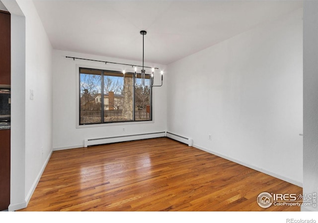 unfurnished dining area featuring a baseboard heating unit, baseboards, wood finished floors, and an inviting chandelier