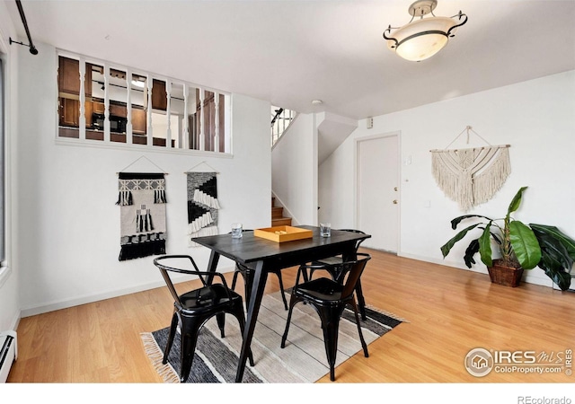 dining space featuring stairway, baseboard heating, wood finished floors, and baseboards