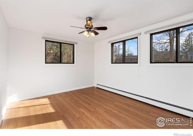 spare room with a baseboard heating unit, ceiling fan, wood finished floors, and baseboards