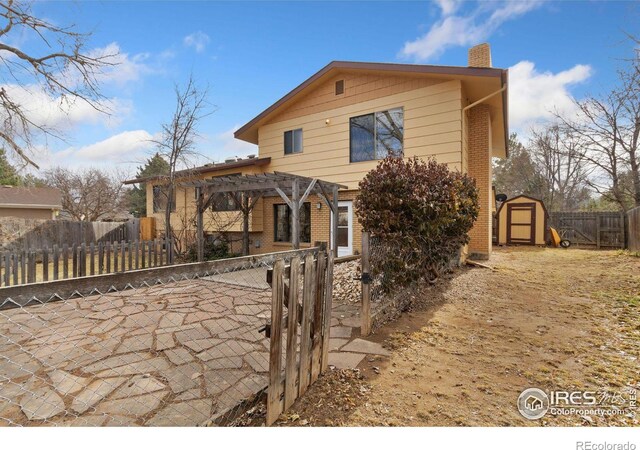 view of front of property featuring brick siding, a chimney, a storage shed, a pergola, and fence private yard