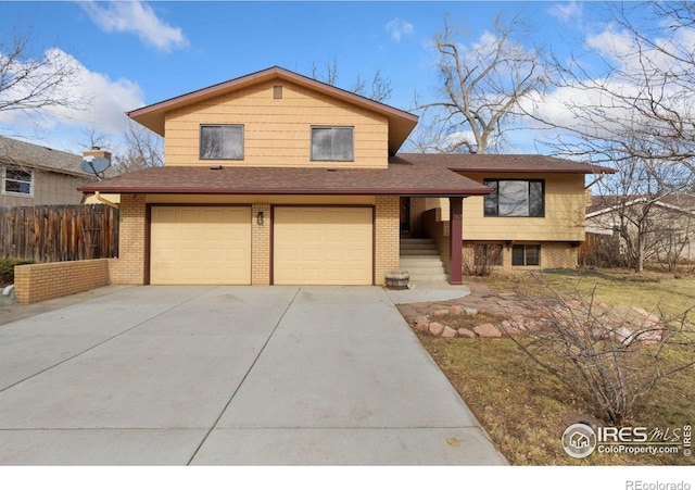 split level home with driveway, an attached garage, fence, and brick siding